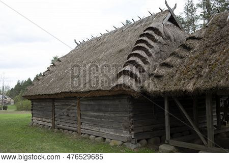 Old Wooden House With Straw, Thatched Roof In Meadow, Open Air. Bungalow Building In Rural Eastern E