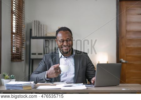 Young African Black Mansmiling Businessman Drinking Coffee And Using Laptop In Office, Sitting At De