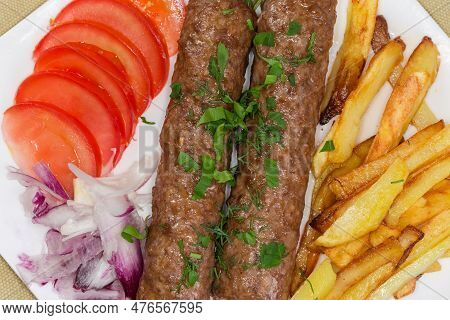 Two Baked Lula Kebab With French Fries And Chopped Vegetables On The Dish, Fragment Top View Close-u