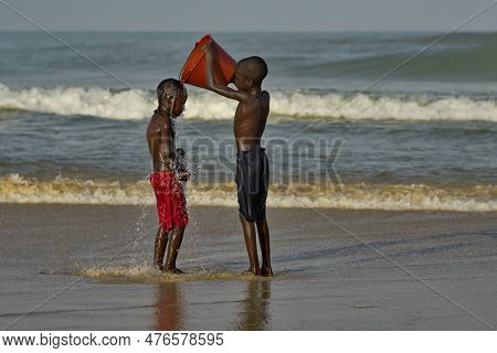 Saint-louis. Senegal. October 11, 2021. Two Village Boys Are Doused With Seawater From A Plastic Buc