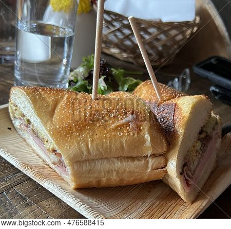 A Delicious Cuban Sandwich Or Muffaletta Is Cut In Half On A Bamboo Plate With Skewers.