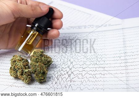 Male Fingers Hold A Bottle Of Cbd Oil Extract, Next To Dry Buds Of Medical Marijuana.  Against The B