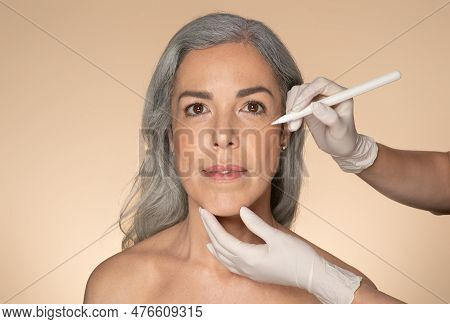 Attractive Senior Caucasian Woman Attending Aesthetic Clinic, Surgeon Making Pre Surgery Marks On Ag