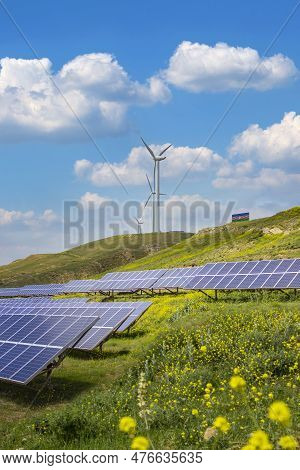 Solar Panels With Wind Turbines Against Mountanis Landscape Against Blue Sky With Clouds