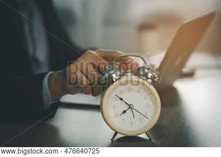 Selective Focus Of Alarm Clock On Desk Near Business Man Using Laptop To Working Overtime For Deadli