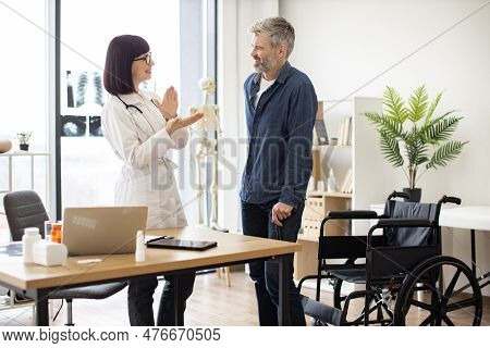 Smiling Female With Stethoscope Clapping While Happy Man Standing On His Feet After Using Wheelchair