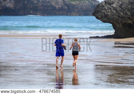 Young Couple Running On Playa De Palombina Las Camaras In Celorio, Green Coast Of Asturias, North Sp