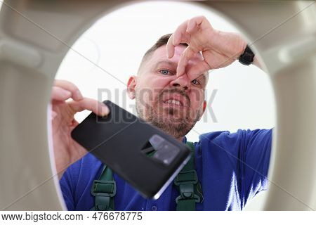 Man With Three-day Stubble Takes Fallen Mobile Phone Out Of Toilet. Male Grimaces Pinching Nose With