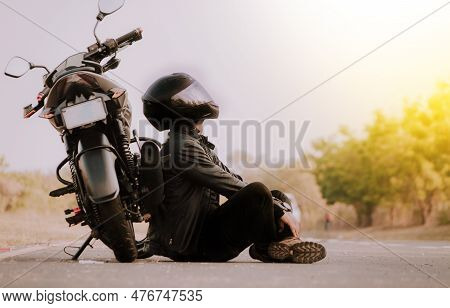 Motorcyclist Sitting Next To His Motorcycle On The Road. Motorcyclist Sitting And Leaning On His Mot