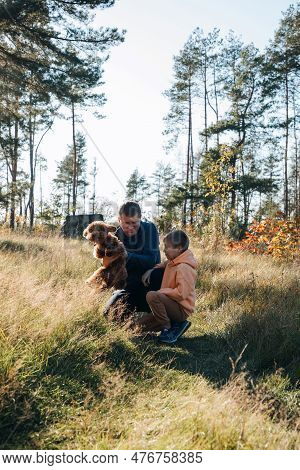 Dad With His Son And A Small Brown Dog Are Playing In A Meadow With Tall Grass. Family Leisure With 