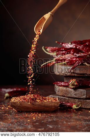 Chilli Flakes Are Poured Into A Wooden Dish. Chilli Flakes And Dried Chili Peppers On A Brown Backgr