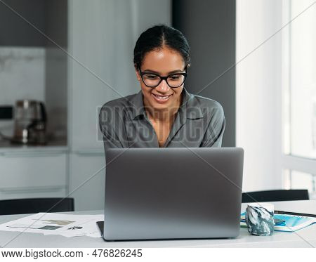Young Female Entrepreneur In Thought Sitting On The Floor In The Kitchen With A Laptop On Her Legs