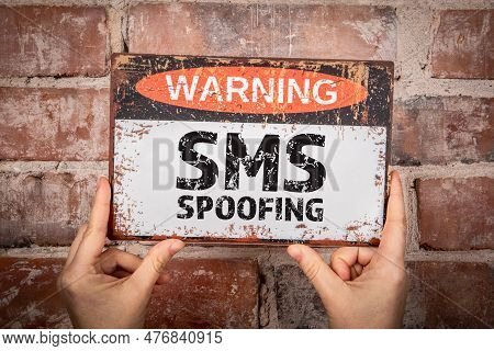 Sms Spoofing. A Woman Is Holding A Warning Sign With Text. Red Brick Background