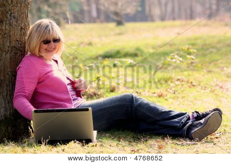 Frau saß mit Laptop gegen Baum