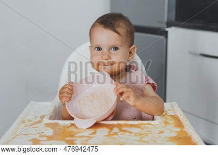 Funny Cheerful Dirty Baby Sits In A Highchair In The Kitchen And Eats Complementary Foods, Holds An 