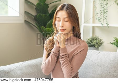 Hopeful Make Wish, Calm Asian Young Woman Belief, Hand In Prayer, Sitting Meditating On Sofa At Home