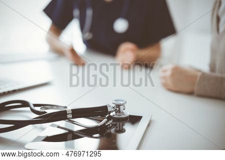 Stethoscope Lying On The Tablet Computer In Front Of A Doctor And Patient At The Background. Medicin
