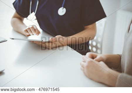 Doctor And Patient Talking To Each Other In Clinic While Sitting And Using Tablet Computer, Close Up