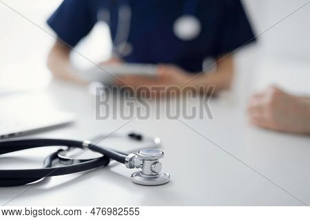 Stethoscope Lying On The Tablet Computer In Front Of A Doctor And Patient At The Background. Medicin