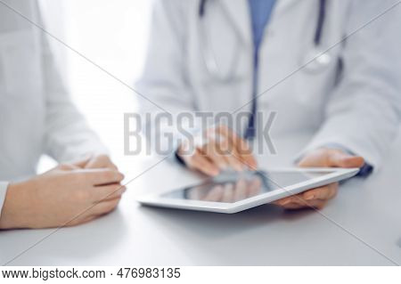 Doctor And Patient Sitting Near Each Other At The Desk In Clinic. The Focus Is On Female Physicians 