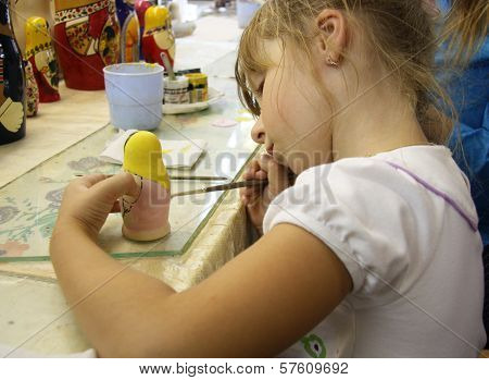 Little girl painting a matrioshka russian doll