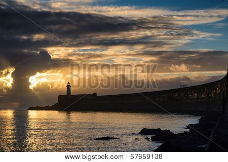Beautiful Vibrant Sunrise Sky Over Calm Water Ocean With Lighthouse And Harbor Wall