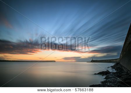 Beautiful Vibrant Sunrise Sky Over Calm Water Ocean With Lighthouse And Harbor Wall