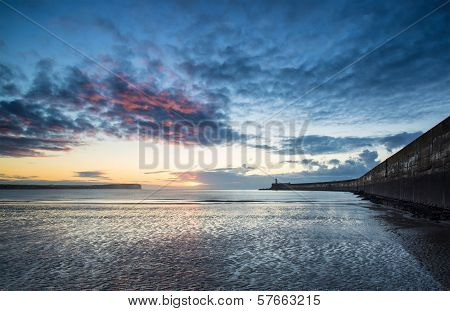 Beautiful Vibrant Sunrise Sky Over Calm Water Ocean With Lighthouse And Harbor Wall