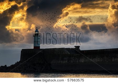 Beautiful Vibrant Sunrise Sky Over Calm Water Ocean With Lighthouse And Harbor Wall