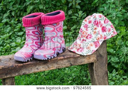 Children Rubber Boots And A Cap On The Bench