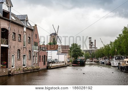 Gouda Netherlands - August 4 2016: Canal of Gouda with vessels and windmill a cloudy day. Gouda is famous for its cheese and its 15th-century city hall.