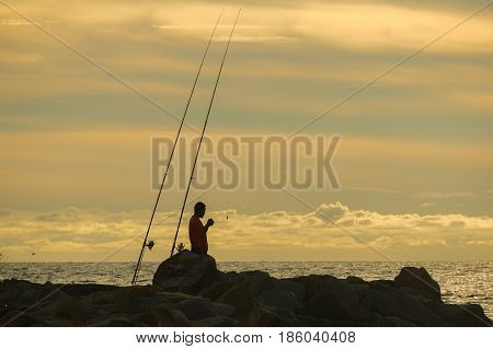 Silhouette of people enjoying the Surf fishing with background of beautiful sunset.Surf fishing is the sport of catching fish standing on the shoreline or wading in the surf.