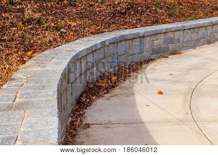 The tone fence on the side of concrete footpath and dry leaves in sunny autumn day