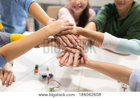 education, children, technology, science and people concept - group of happy kids building robots l at robotics lesson and holding hands together