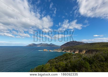 View from Cape Tourville Lighthouse lookout - Seascape photo, cliff coastline, green mountain, blue sky at Freycinet National Park, Tasmania, Australia 