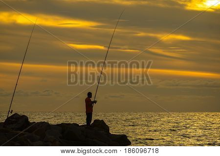 Silhouette of people enjoying the Surf fishing with background of beautiful sunset.Surf fishing is the sport of catching fish standing on the shoreline or wading in the surf.