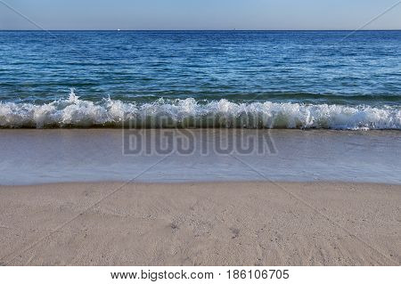 Wave breaking by the beach at the Portinho da Arrabida beach in Portugal; Concept for summer vacations and travel in Portugal