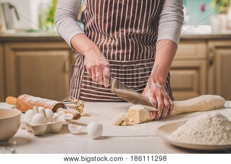 Close-up view of two woman's hands cut knife dough. A woman in a striped apron is cooking in the kitchen