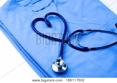 Medical stethoscope twisted in heart shape lying on patient medical history list and blue doctor uniform closeup.