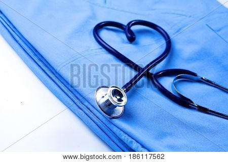 Medical stethoscope twisted in heart shape lying on patient medical history list and blue doctor uniform closeup.
