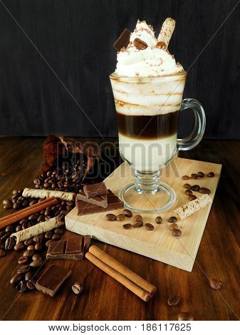 Coffee cocktail with whipped cream in an Irish coffee mug surrounded by coffee beans, cinnamon and chocolate bars