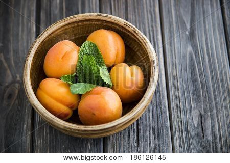 Ripe orange apricots in a clay bowl on a wooden table