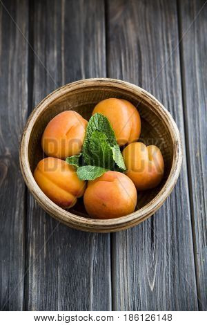 Ripe orange apricots in a clay bowl on a wooden table