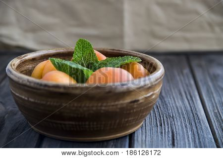 Ripe orange apricots in a clay bowl on a wooden table