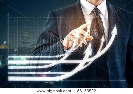 Businessman pointing at creative business chart with upward arrows on night city background. Financial growth concept