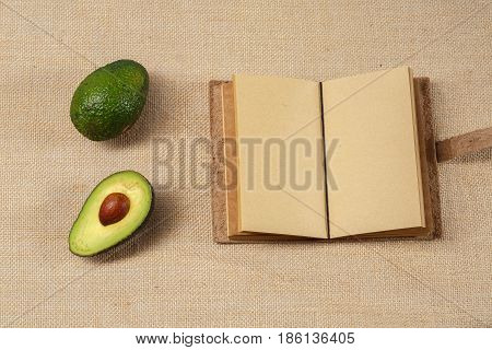 Fresh Avokado and Clear Notebook lying on a brown old sackcloth surface