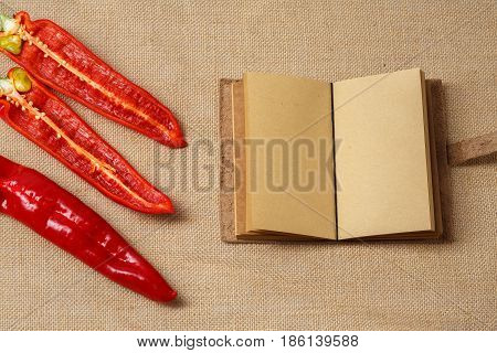 Red Chili Pepper and Clear Notebook lying on a brown old sackcloth surface