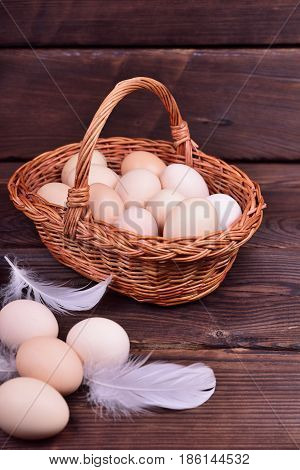 Yellow chicken eggs in a wicker basket on a brown wooden surface close up