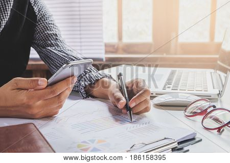 Business woman working with smart phone and discussing the analysis charts or graphs on modern White office desk table .Business concept.