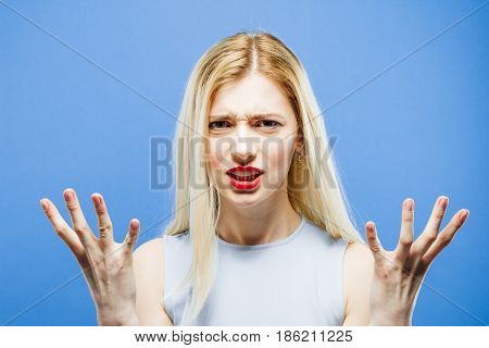 Frustrated Blonde with Long Hair on Blue Background in Studio. Emotional Girl Wearing Dress is Looking at the Camera with Sadness in the Eyes.